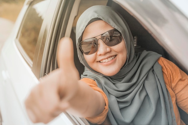 Aziatische moslimvrouw glimlacht tijdens het rijden, heeft plezier in de vakantie, rijdt in de auto en deelt duimen omhoog.