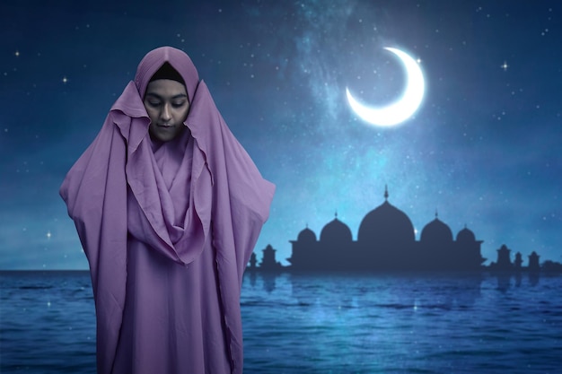 Aziatische moslimvrouw in sluier in gebedspositie salat met de achtergrond van de nachtscène