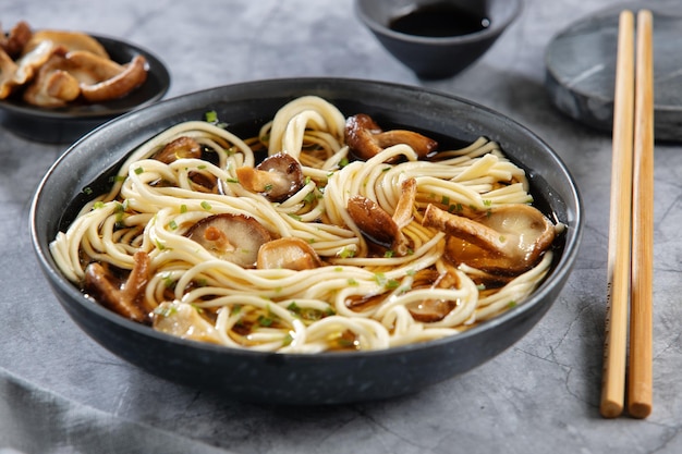 Aziatische noedelsoep met shiitake van champignons geserveerd in een donkere kom. Detailopname