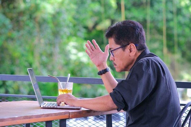 Aziatische ongelukkige zakenman die onaangenaam naar zijn laptop kijkt