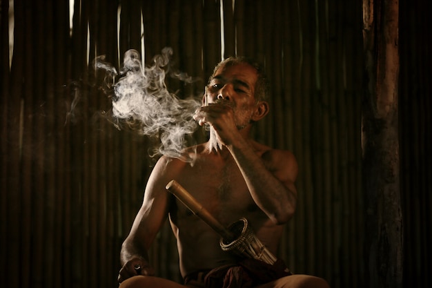 Aziatische oude man roken sigaret en de rook vrijgegeven uit de mond tegen dark