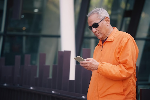 Foto aziatische oude oudere senior man ouderen met behulp van mobiele smartphone mobiele telefoon buiten volwassen pensionering levensstijl