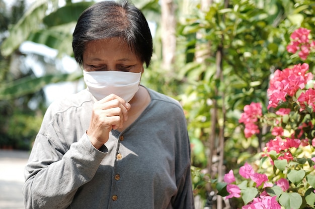 Aziatische oude vrouw die een wit stoffen masker draagt ter voorkoming van het Covid-19- of Corona-virus en hoesten in Thailand en bescherming voor luchtverontreinigingswaarde Pm 2,5. Gezondheid en geneeskunde van ouderen concept