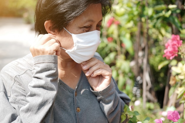 Aziatische oude vrouw die een wit stoffen masker draagt ter voorkoming van het Covid-19- of Corona-virus in Thailand en bescherming voor luchtverontreinigingswaarde Pm 2,5