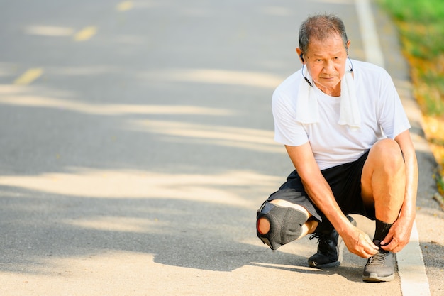 Aziatische oudere man of senior loper Bind je schoenveters om je klaar te maken om te joggen. In de buitenlucht joggen en wandelen in het park.