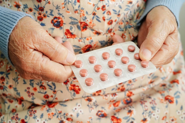 Aziatische oudere vrouw die pilmedicijn in de hand houdt, sterk gezond medisch concept