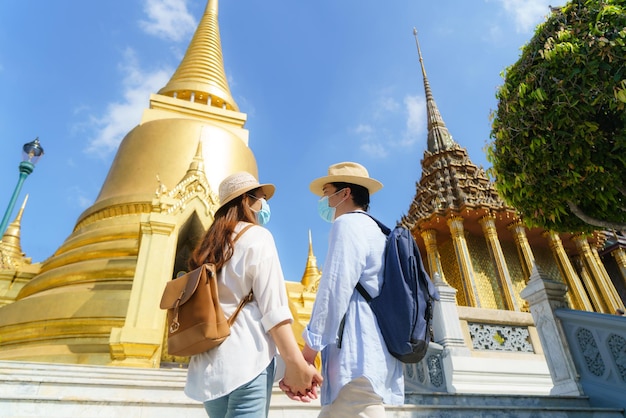 Aziatische paar gelukkige toeristen reizen met een masker om te beschermen tegen Covid-19 op hun vakantie in de Wat Phra Kaew-tempel in Bangkok, Thailand