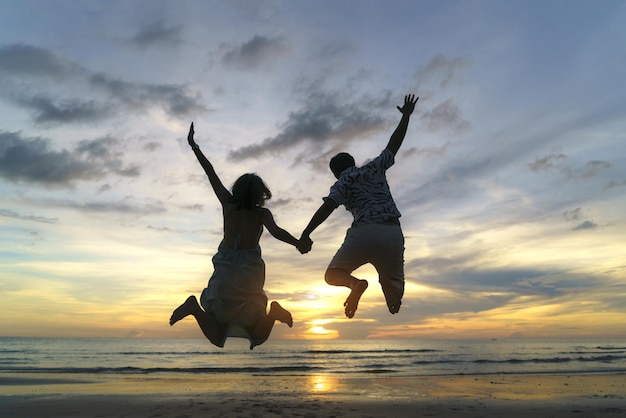 Aziatische paar springen op het strand in de buurt van zee met prachtige zonsondergang