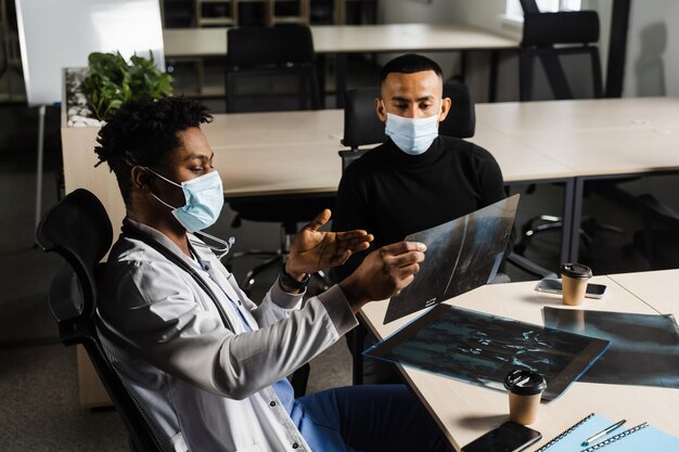 Aziatische patiënt bij Afrikaanse doktersafspraak Fractuur van de botten van de voet Zwarte chirurg die röntgenfoto toont aan patiënt