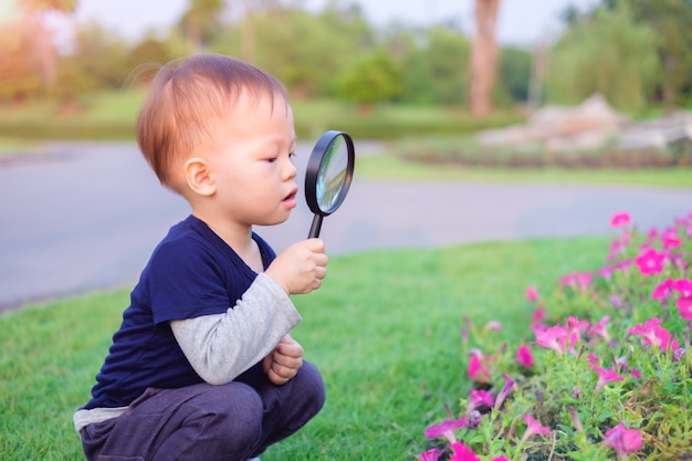 Foto aziatische peuterjongen die milieu onderzoekt door door een vergrootglas in zonnige dag te kijken