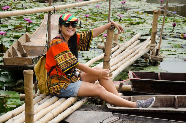 Aziatische reizigers Thaise vrouw reizen bezoek en zitten bamboe brug om foto te nemen met houten boot drijvend met waterlelie in vijver in de tuin van Red Lotus drijvende markt in Nakhon Pathom Thailand