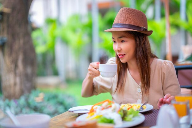 Aziatische reizigersvrouw die ontbijtbuffet eet in het hotelrestaurant op het buitengebied met koffie