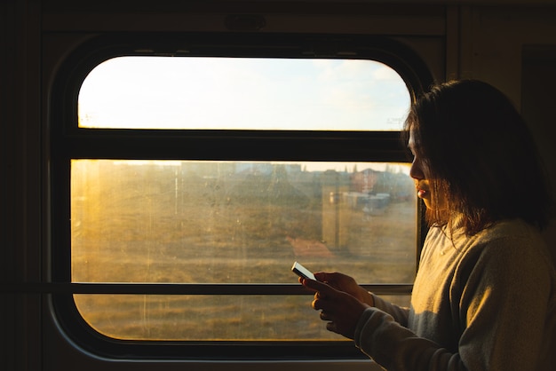 Aziatische reizigersvrouw kijkt naar slimme mobiele telefoon naast het raam van een rijdende trein