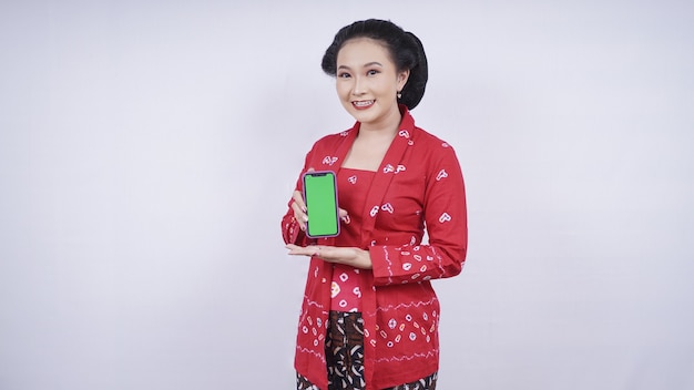 Aziatische schoonheid in kebaya die het smartphonescherm toont dat op witte achtergrond wordt geïsoleerd