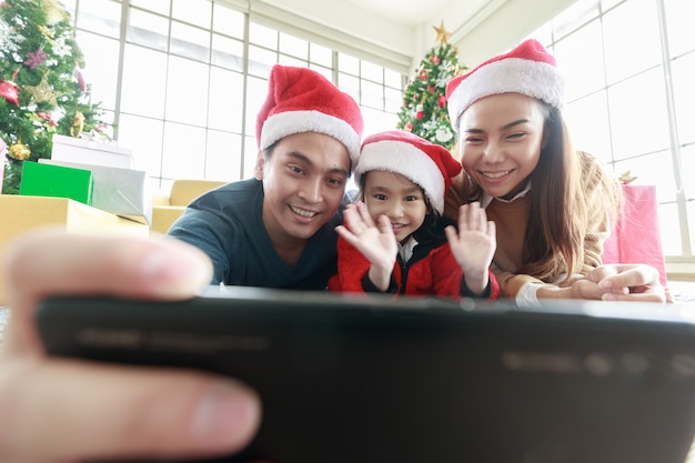 Aziatische Selfie met smartphone Foto maken. Gelukkig jong gezin met kinderen leuk om Kerstmis te vieren. Kersttijd. Mijn vader, moeder en dochter met kerstmutsen liggen vooraan Geschenkdoos thuis.