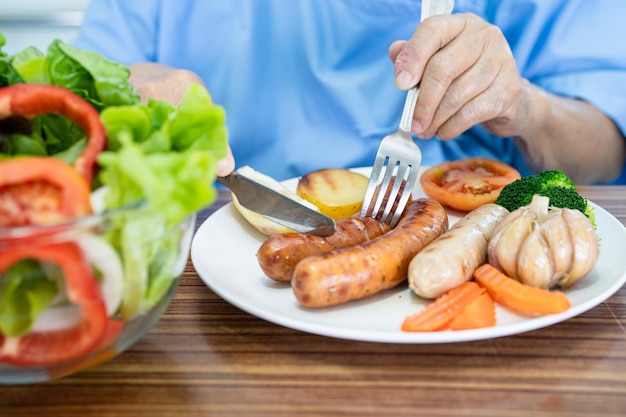 Aziatische senior of oudere oude dame vrouw patiënt eet zalm steak ontbijt met plantaardig gezond voedsel zittend en hongerig op bed in het ziekenhuis