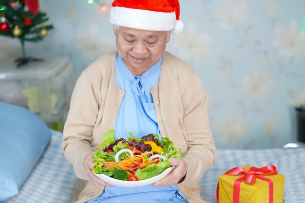 Aziatische senior of oudere oude dame vrouw patiënt met kerstman helper hoed en plantaardig voedsel erg blij in kerst en nieuwjaarsfeest festival vakantie feest in het ziekenhuis.