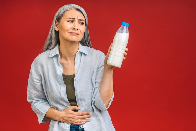 Aziatische senior volwassen oude vrouw die melk drinkt geïsoleerd op rode achtergrond Allergie voor lactose smakeloos voedsel maagpijn