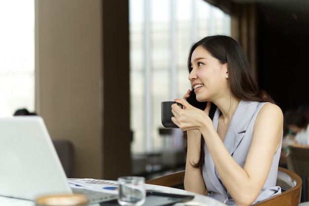 Aziatische slimme mooie meisjes sprekende zaken op mobiele telefoon en holdingskop van koffiezitting in koffiewinkel.