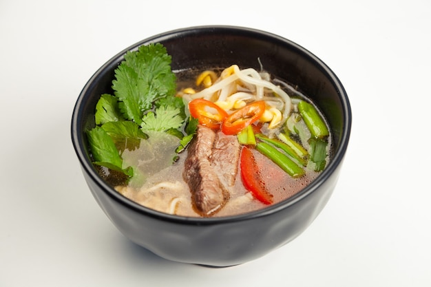 Aziatische soep met rundvlees en Udon-noedels in een zwarte kareliaan.