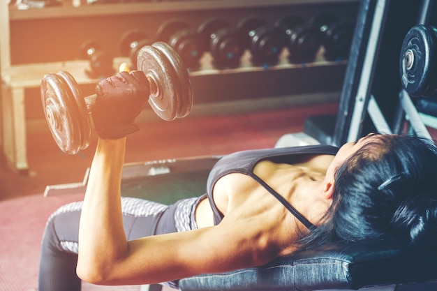 Aziatische sportenvrouw die oefeningen met domoorgewichten doen in gymnastiek