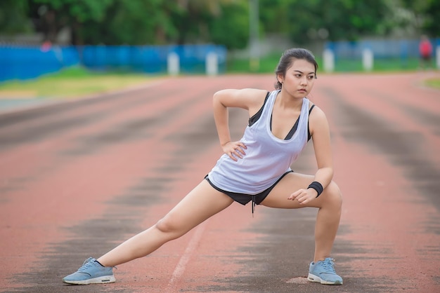 Aziatische sportieve vrouw die het lichaam uitrekt en frisse lucht ademt in het park Thailand mensenFitness en oefeningsconcept Joggen in de baan