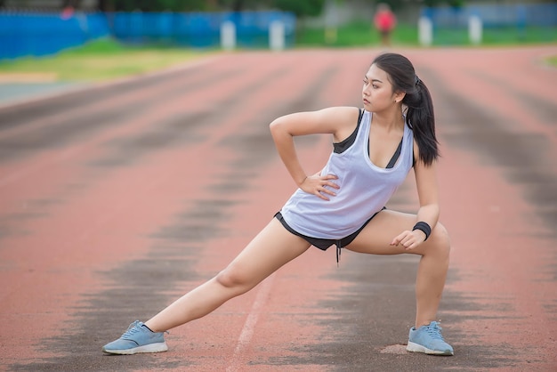 Aziatische sportieve vrouw die het lichaam uitrekt en frisse lucht ademt in het park Thailand mensenFitness en oefeningsconcept Joggen in de baan