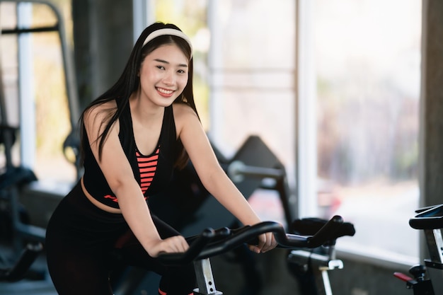 Aziatische sportvrouw die traint op een fiets in de sportschool vastberadenheid om cardio af te vallen, maakt haar gezonde hometrainer vrouw fitness sport concept