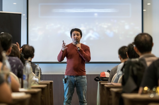 Aziatische spreker met casual pak op het podium over het presentatiescherm in het bedrijf of educatio