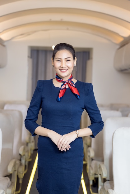 Aziatische stewardess poseren met glimlach in het midden van het gangpad in de passagiersstoel van het vliegtuig op de achtergrond