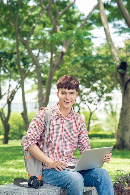 Aziatische student die laptop gebruikt die in park zit