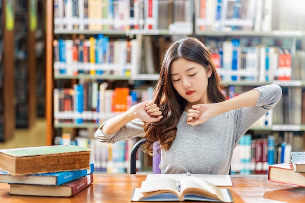 Aziatische student in casual pak lezen en rekoefeningen doen in de bibliotheek van de universiteit