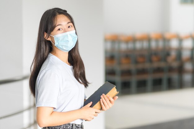 Aziatische studente in ontspannen casual terug naar school met medisch gezichtsmasker op de campus