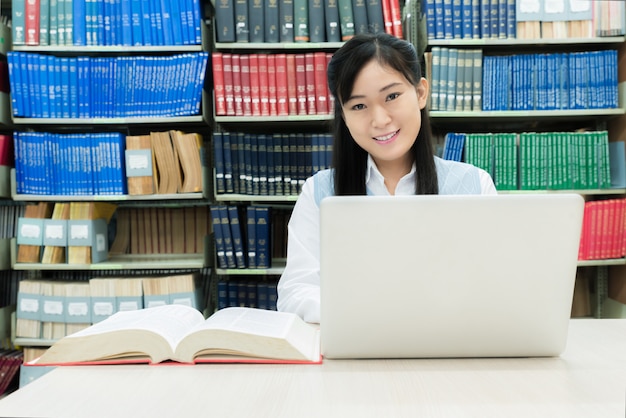 Aziatische studente met laptop en boeken die bij bibliotheek op universiteit werken.