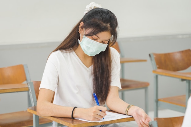 Aziatische studenten die terug naar school gaan, dragen een gezichtsmasker en houden afstand bij het studeren in de klas