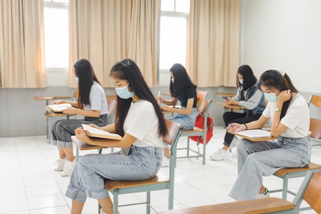 Aziatische studenten die terug naar school gaan, dragen een gezichtsmasker en houden afstand bij het studeren in de klas