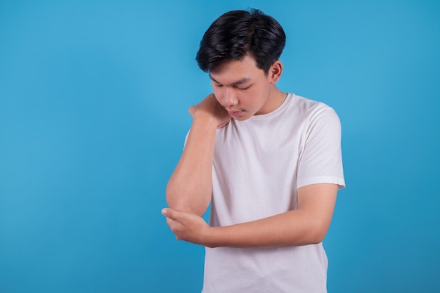 Aziatische tiener draagt een wit t-shirt met pijn in een gewonde elleboog op een blauwe achtergrond Gezondheidszorg en armpijnconcept