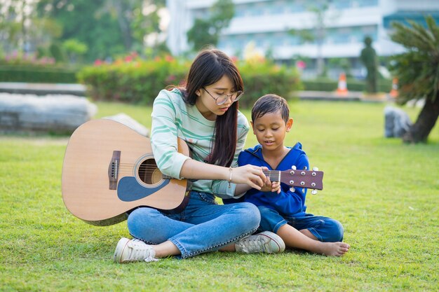 Aziatische tiener leert gitaar voor de jongen met liefdevol en plezier in de groene weiden