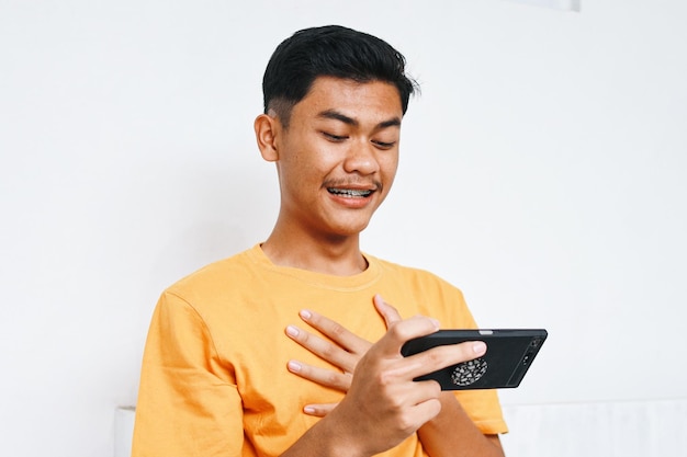 Aziatische tiener met beugels die met geschokte uitdrukking naar zijn smartphone kijkt.