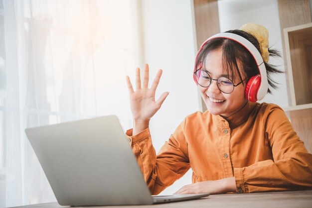 Aziatische tienerstudenten in een gele jurk die een koptelefoon dragen, communiceren via videoconferenties voor online leren. In een videoconferentiegesprek via apps. nieuw normaal concept