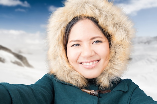 Aziatische toerist die een groene jas draagt met een sneeuwbergachtergrond