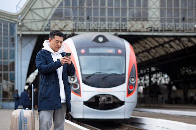 Aziatische toeristen die accommodatie thuis boeken met behulp van mobiele telefoon, passagier arriveert met de trein naar nieuwe stad