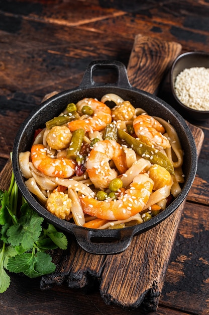 Aziatische Udon roerbaknoedels met garnalen en garnalen in een pan. Donker hout