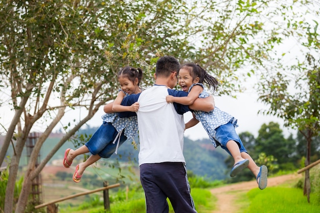 Aziatische vader die twee kindmeisjes draagt ​​en rond met pret in het park ronddraait