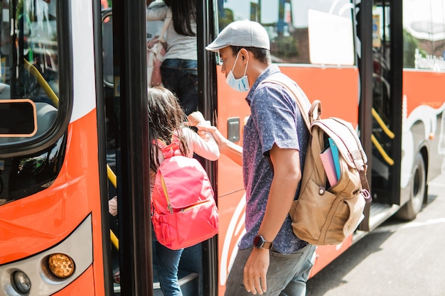 Aziatische vader die zijn dochter naar school brengt met het openbaar vervoer per bus met een gezichtsmasker op