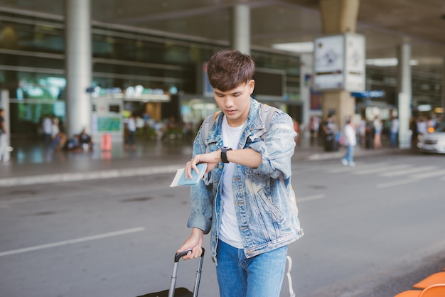 Aziatische verwarde mannelijke toerist kijkt op zijn horloge op de luchthaven