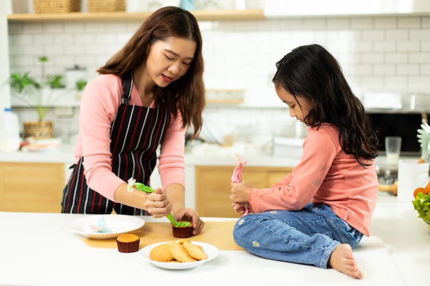 Aziatische voorschoolse jongen maakt taart koken in de keuken Moeder bereidt decoratie mooi met plezier voor op cupcake voor verjaardagszus Crème puinhoop over haar gezicht mond voelt gelukkig kopieerruimte