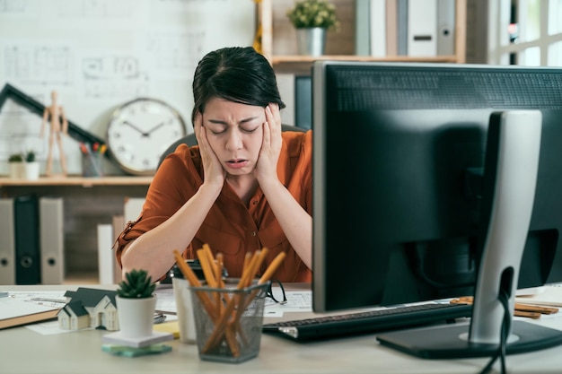 aziatische vrouw architect ingenieur die oren bedekt en irritant hard geluid negeert, stopt oren om te voorkomen dat ze geluid horen. Lawaaierige muziek probleem. fronsend overstuur vrouwelijke ontwerper ziek vermoeide hand op gezicht