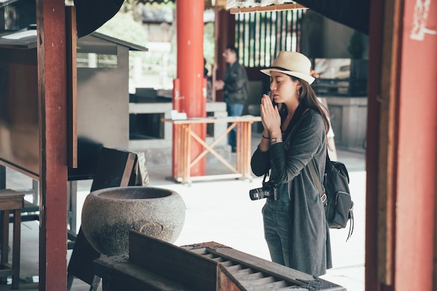 aziatische vrouw backpacker toerist met camera ervaring japanse traditionele cultuur bidden voor zegeningen hand in shitennoji tempel. jong meisje elegante gesloten ogen staan in vreedzaam shinto osaka japan