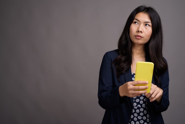 Aziatische vrouw blauwe jurk en cardigan trui dragen tijdens het gebruik van mobiele telefoon tegen grijze ruimte